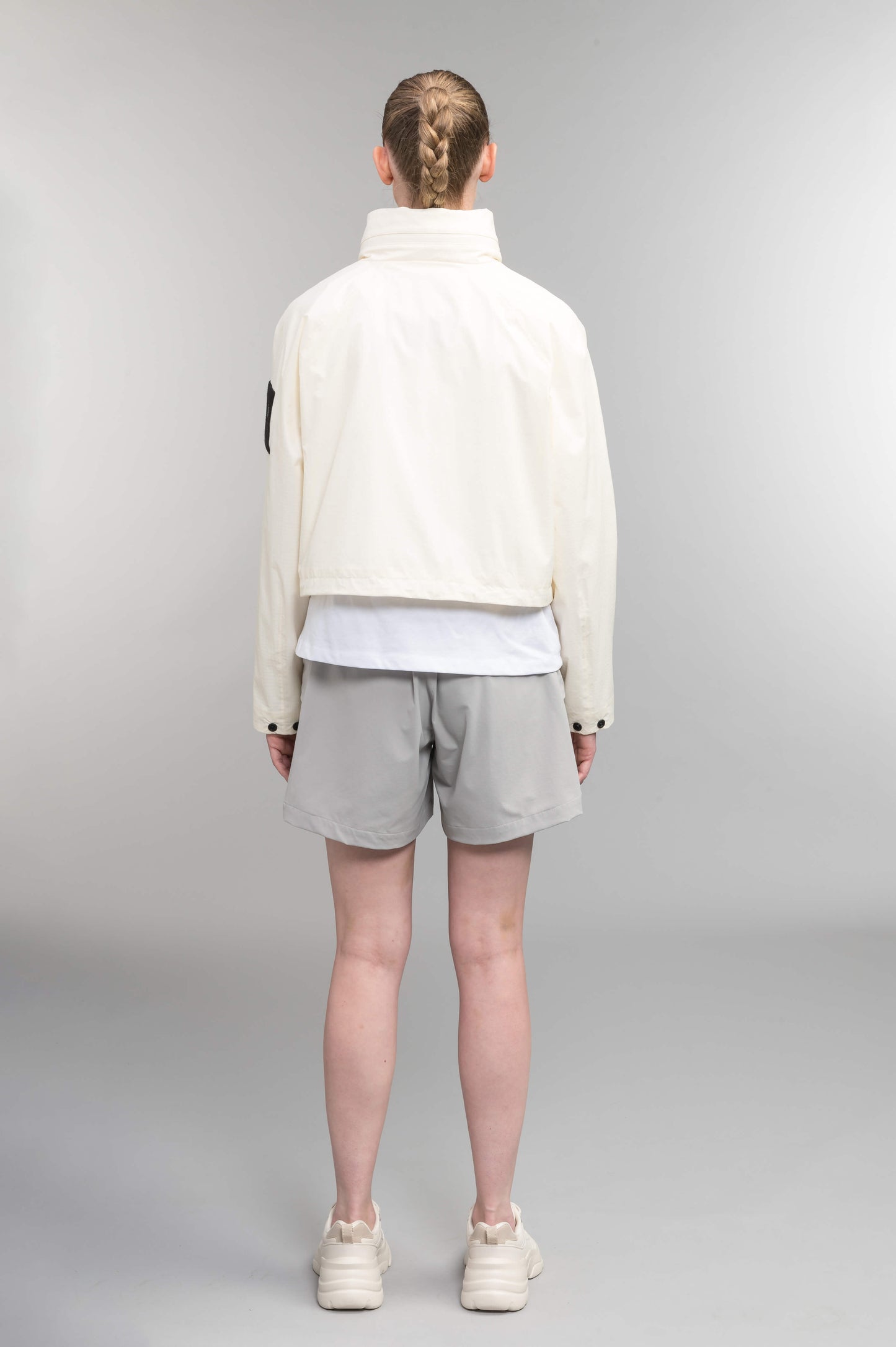 Epsie Women's Cropped Rain Jacket in Chalk crafted from premium recycled polyester ripstop with a DWR coating and taffeta nylon lining. Features a hidden packaway hood stored in the collar, two-way waterproof front zipper, seam-sealed construction, underarm zip ventilation, adjustable drawcord hem, zippered waist patch pockets, and an interior chest pocket for secure storage. Machine washable. Designed in Canada.