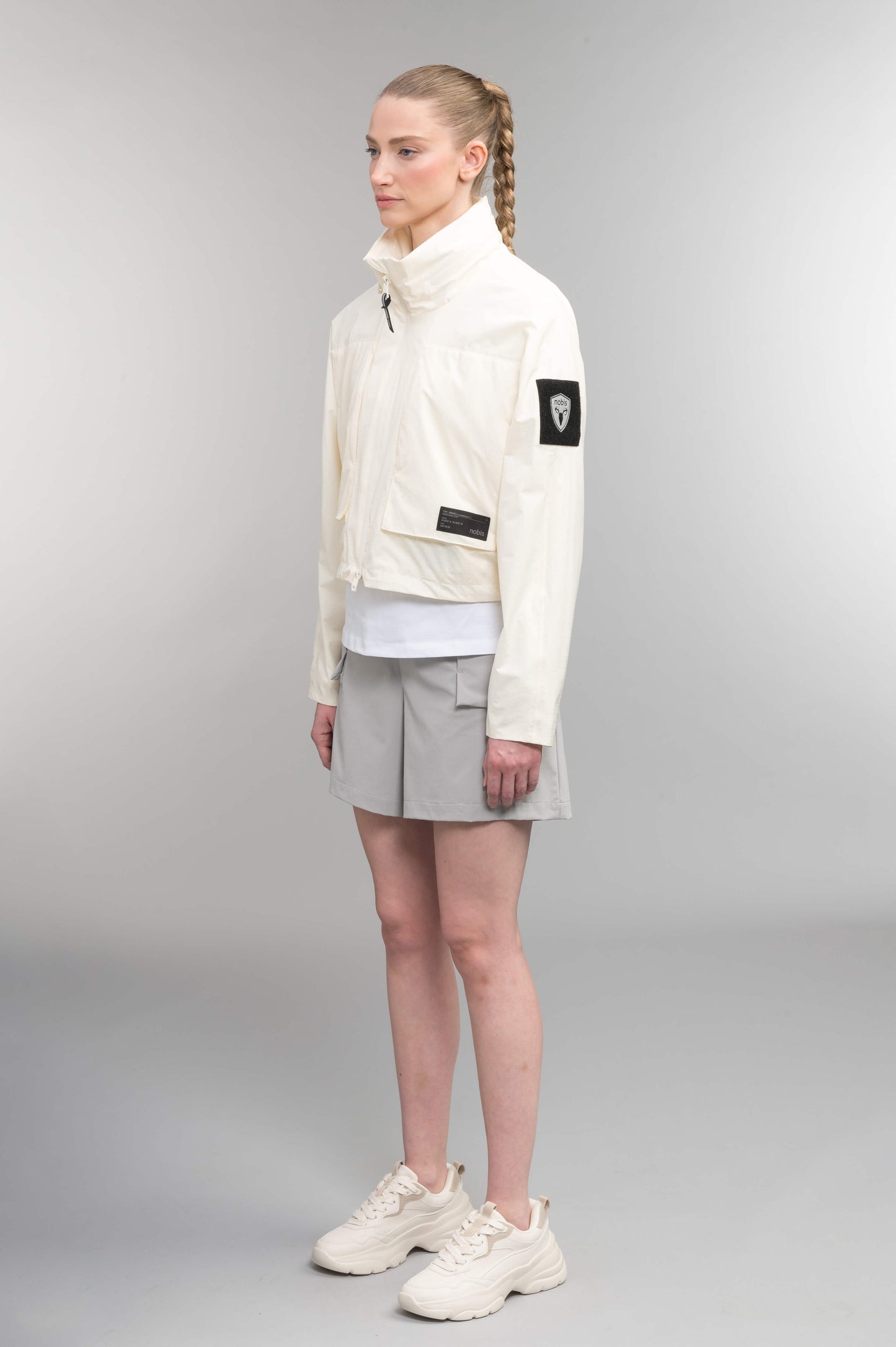 Epsie Women's Cropped Rain Jacket in Chalk crafted from premium recycled polyester ripstop with a DWR coating and taffeta nylon lining. Features a hidden packaway hood stored in the collar, two-way waterproof front zipper, seam-sealed construction, underarm zip ventilation, adjustable drawcord hem, zippered waist patch pockets, and an interior chest pocket for secure storage. Machine washable. Designed in Canada.