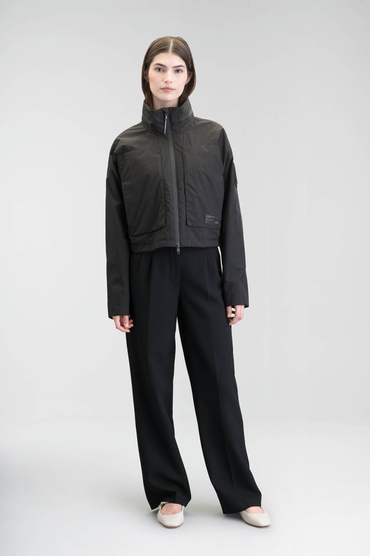 Epsie Women's Cropped Rain Jacket in Black crafted from premium recycled polyester ripstop with a DWR coating and taffeta nylon lining. Features a hidden packaway hood stored in the collar, two-way waterproof front zipper, seam-sealed construction, underarm zip ventilation, adjustable drawcord hem, zippered waist patch pockets, and an interior chest pocket for secure storage. Machine washable. Designed in Canada.