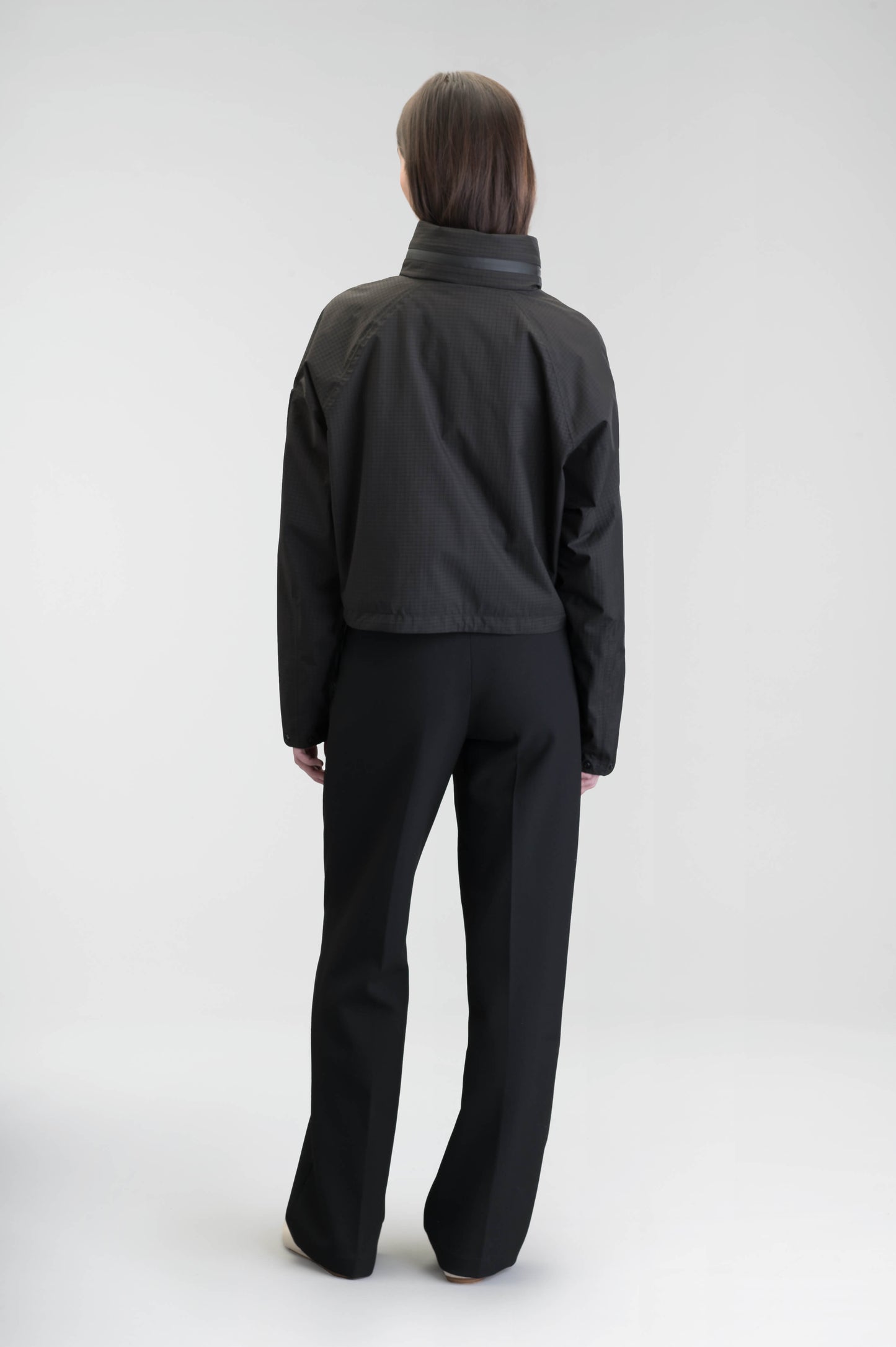 Epsie Women's Cropped Rain Jacket in Black crafted from premium recycled polyester ripstop with a DWR coating and taffeta nylon lining. Features a hidden packaway hood stored in the collar, two-way waterproof front zipper, seam-sealed construction, underarm zip ventilation, adjustable drawcord hem, zippered waist patch pockets, and an interior chest pocket for secure storage. Machine washable. Designed in Canada.