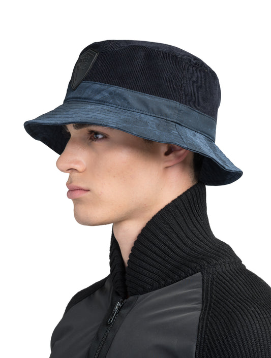 Kaia Unisex Tailored Bucket Hat in a 100% cotton corduroy and 3-ply micro denier fabrication, unstructured crown, black leather Nobis shield logo on crown front, and small flap pocket on the right side crown, in Navy